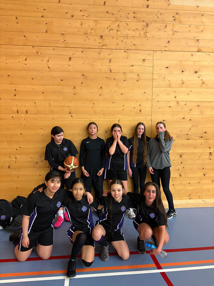 Indoor group photo of seven volleyball players in black uniforms posing in a gym