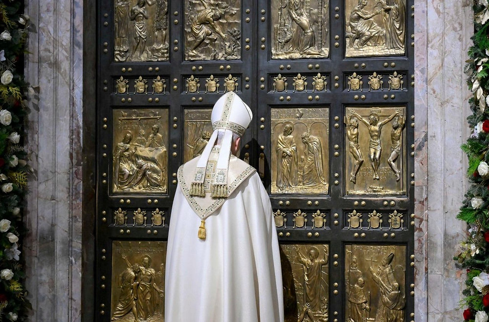 Religious figure in white vestments facing ornate black-and-gold church doors