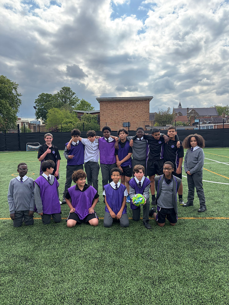 Group of students and adults posing on a sports field in purple and black uniforms under a cloudy sky