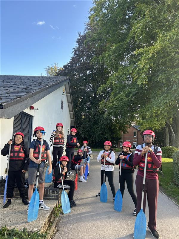 Group of paddleboarders in red helmets posing with blue paddles outside a building