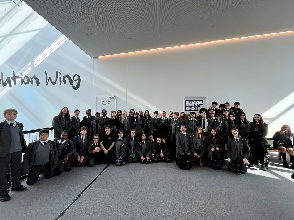 Large group in black formalwear posing indoors under a skylight, with “Aviation Wing” on the wall.