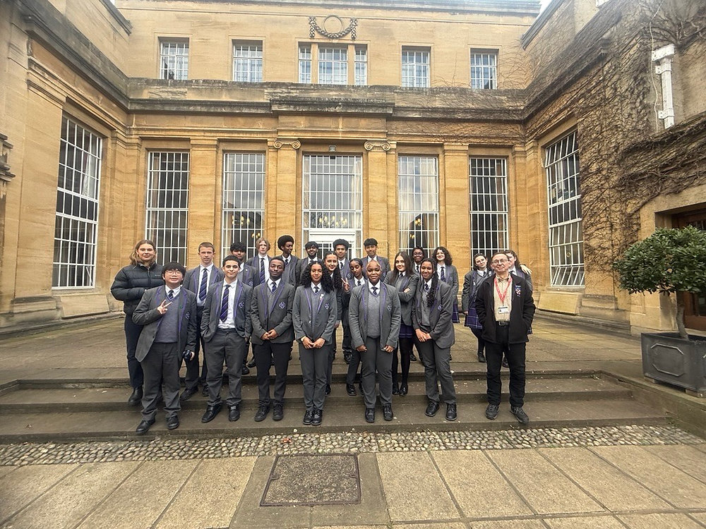 Group of people in suits posing outside a historic stone building with large windows.