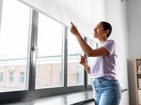 woman manually adjusting a large white roller shade