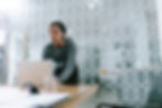 Photo of young African American woman at head of boardroom table. In front of her is an open laptop. She is looking up in the distance ahead of her.