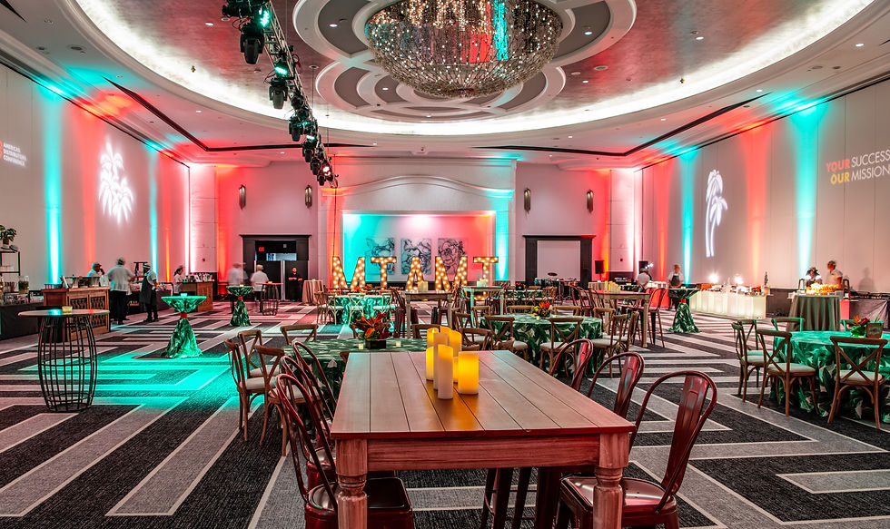 Spacious event hall with red and teal lights, a "MIAMI" sign, tables with candles, and buffet stations. Text on wall: "YOUR SUCCESS OUR MISSION."