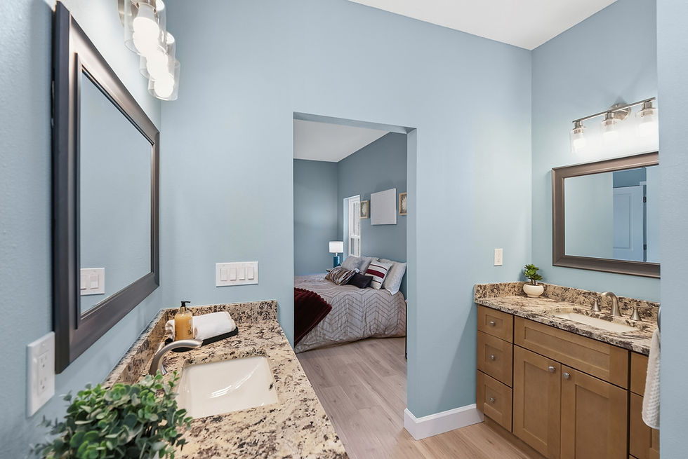 Bright blue bathroom with granite vanity and mirrors, looking through doorway to a neatly made bedroom.