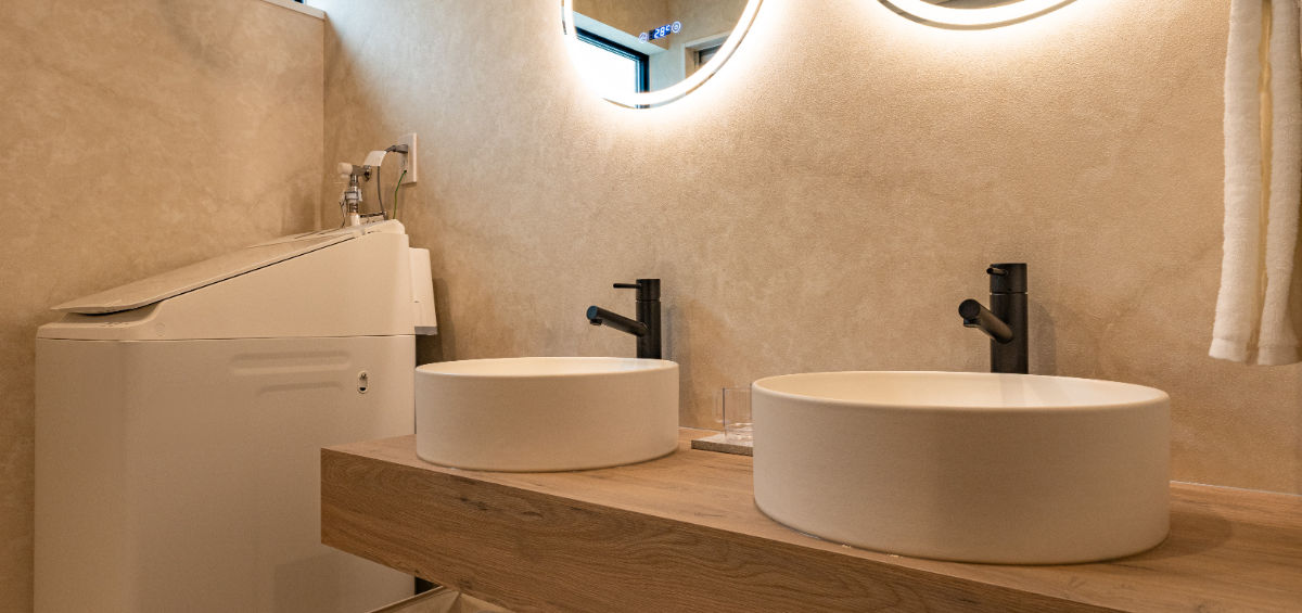 Modern bathroom with double sinks, illuminated mirrors, and wooden vanity.