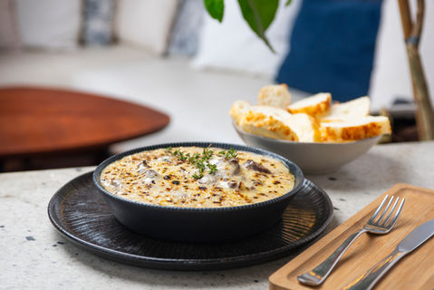 Mignon com catupiry gratinado, servido em tigela preta sobre prato rústico, acompanhado de pães artesanais em bowl ao fundo.