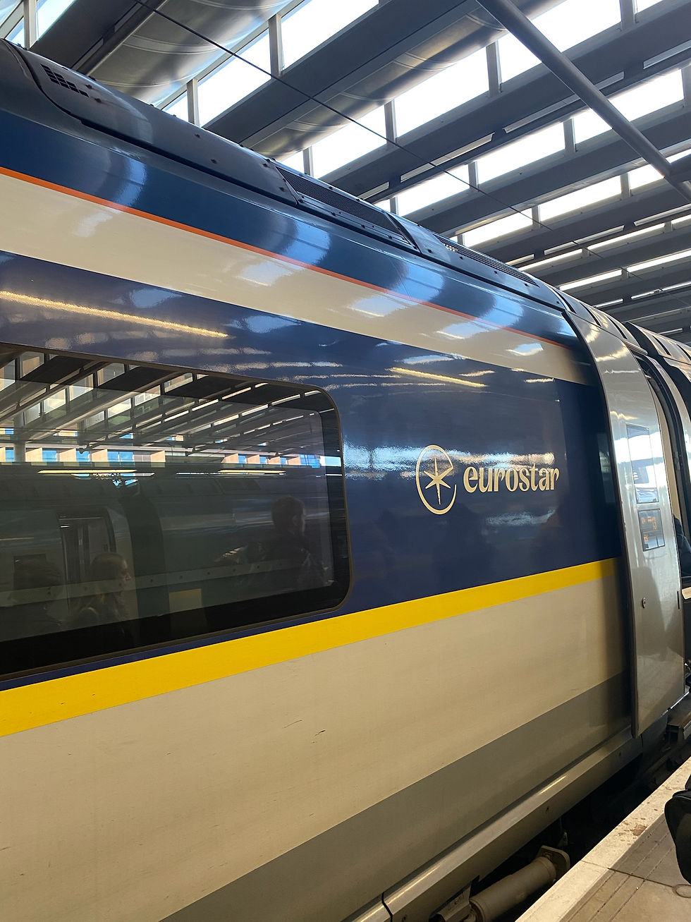 Eurostar train at a station with a blue, white, and yellow exterior. The logo and name "eurostar" are visible. Windows reflect passengers.
