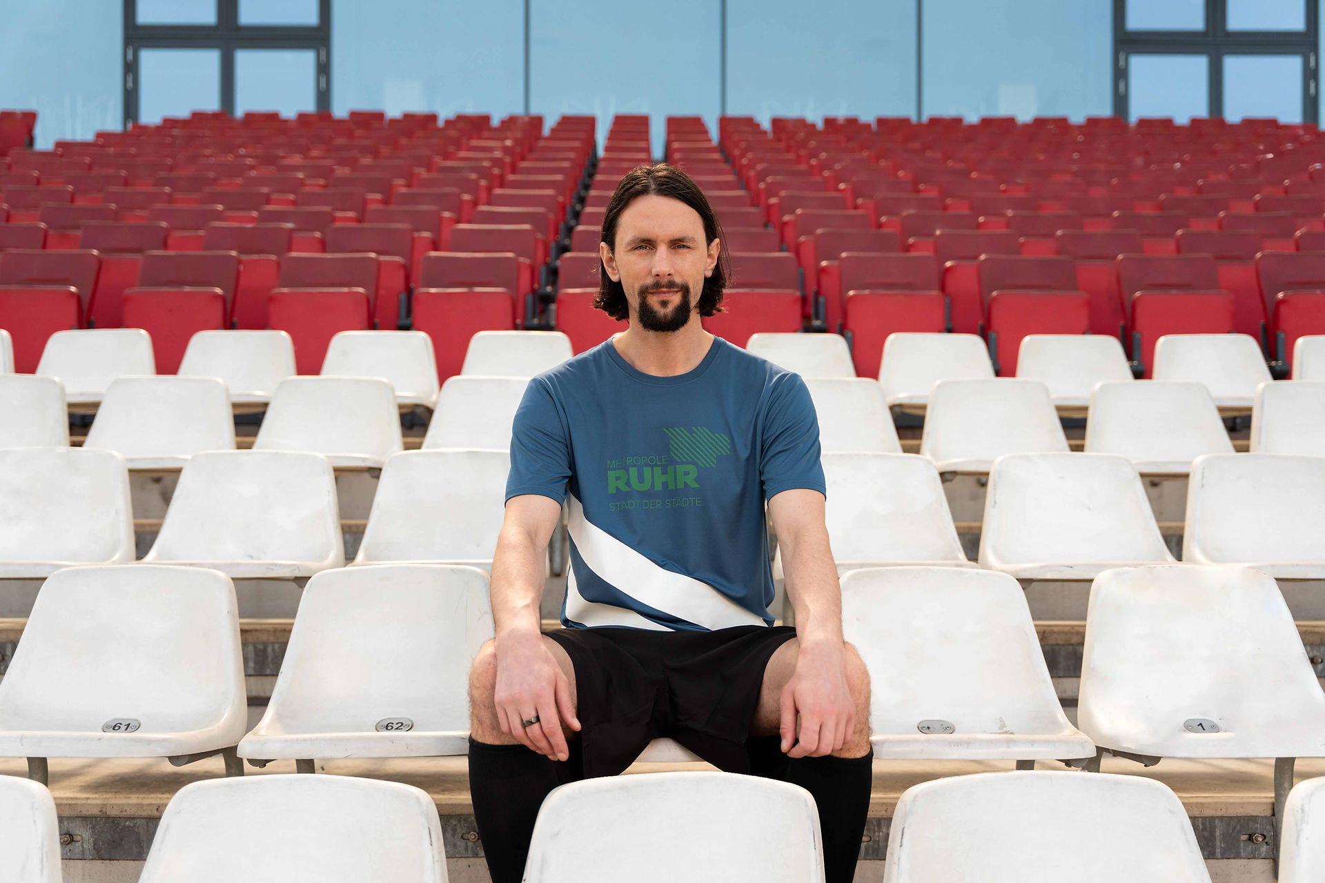 Imagefilm Kampagne von Twinematics mit Neven Subotić im Fußballstadion. Neven Subotić sitzt auf der Tribüne und guckt frontal in die Kamera.