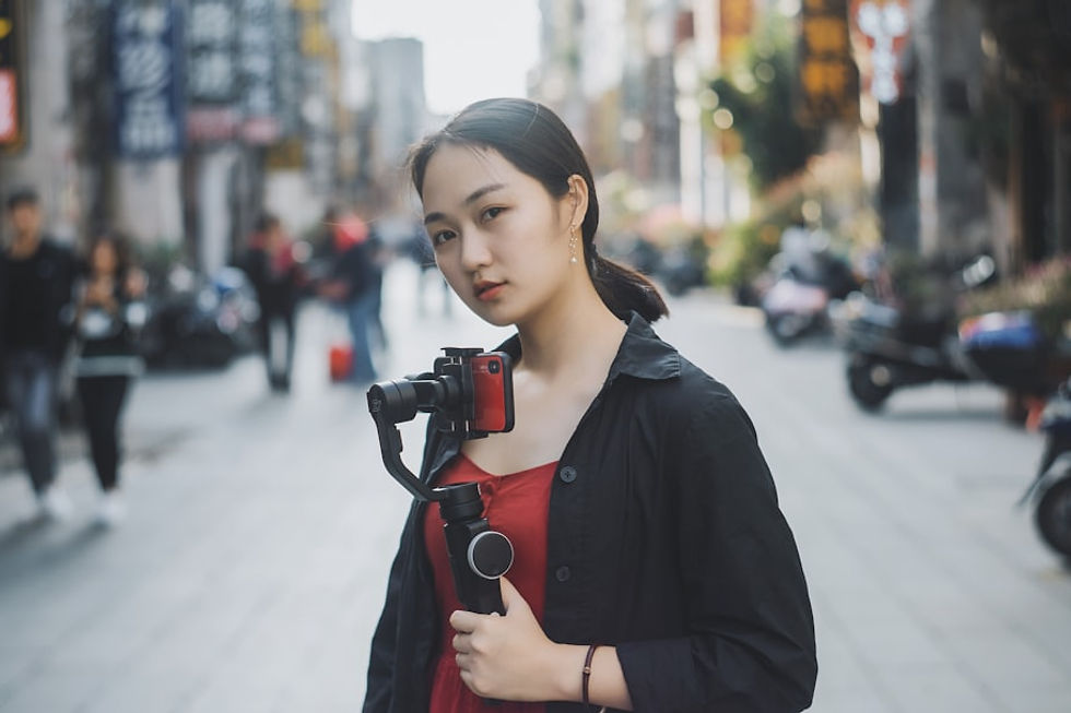 woman holding gimbal with camera standing in the middle of the road near people and motorcycles