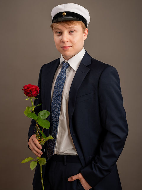 Nuori mies ylioppilaslakissa, tummassa puvussa ja kravatti kaulassa, pitelee punaista ruusua kädessään. Kuva otettu Kuvaajankulman studiossa Lappeenrannassa.