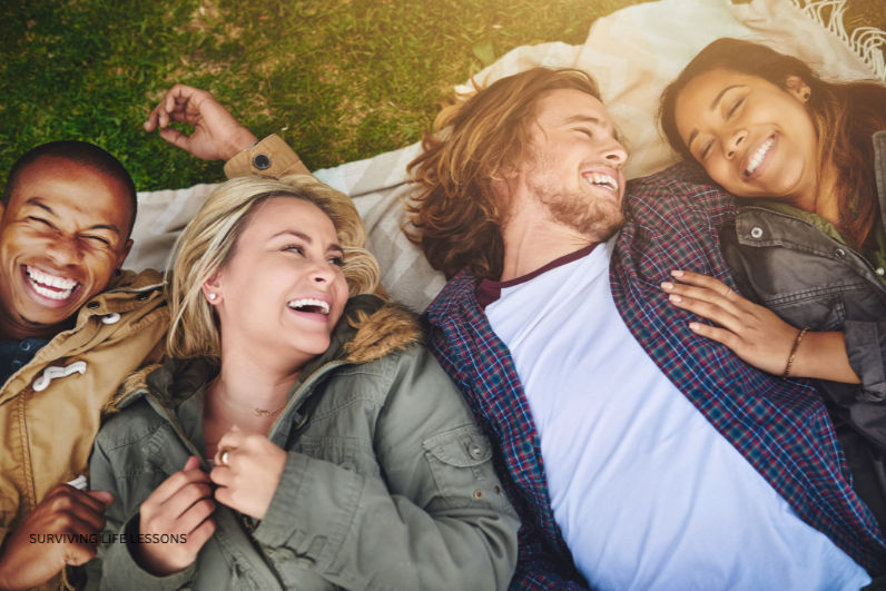 A group of friends share laughter while lying on a blanket outdoors, capturing a joyful moment of connection and carefree happiness.