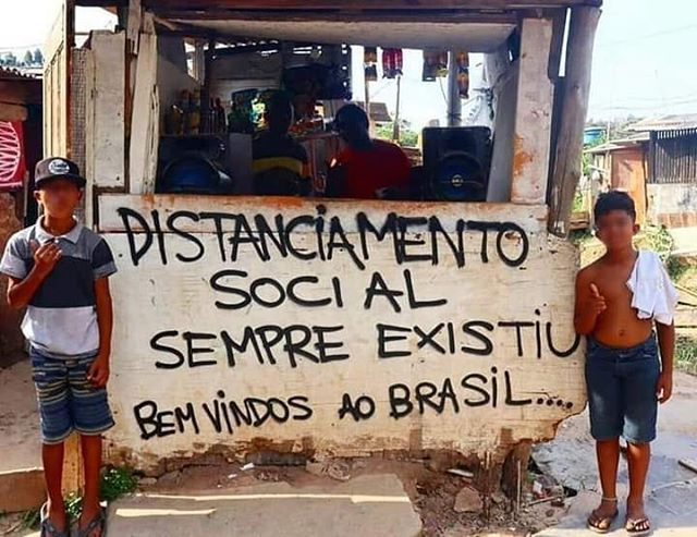 Dois meninos pretos ao lado de um cartaz com crítica social a realidade da periferia brasileira