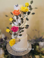 Summer Breeze is a luxurious four-tier wedding cake designed to serve approximately 100 guests. Finished with crisp white fondant over a smooth ganache finish, the design features an elegant cascade of individually handcrafted sugar roses in vibrant summer tones, delicately wired foliage and edible butterflies that create a sense of movement throughout the cake. Each flower is made by hand, making every cake unique and a true edible work of art.