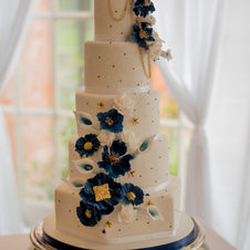 Five tier tall white background wedding cake, with blue embellishments and blue flowers