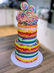 Rainbow colour two tier birthday cake with bows, stripes and bright lollipops