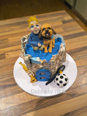 Music sheet covered cake with a trumpet, football and tennis racket around the bottom then on the top a cute cariature of a boy and his dog