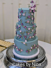 Dusky blue base colour three tier cake, with small sugar flowers in dusky pink, lilac, and purple, with green leaves - The Elvetham