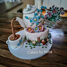3d edible teapot that is dripping tea out of its spout into an edible tea cupcake, with sugar flowers, and gardening decorations