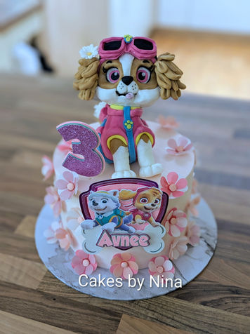 Stunning handmade paw patrol model on a white base cake with lots of flowers