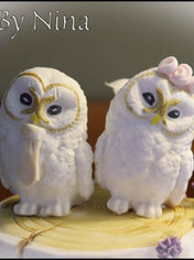 Handcrafted pair of white owl wedding cake toppers with gold facial detailing and pink sugar flower by Cakes by Nina