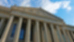 Exterior of the U.S. National Archives building with tall columns and intricate carvings. Blue sky and clouds in the background.