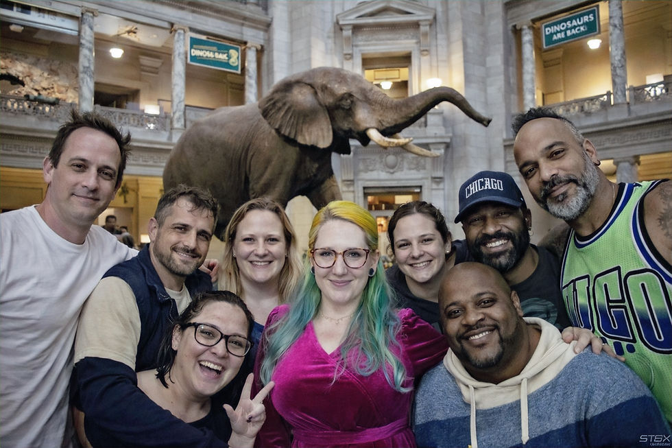 Grand domed building with a white facade, trees, and a path leading to the entrance. People walk along the path under a clear blue sky.