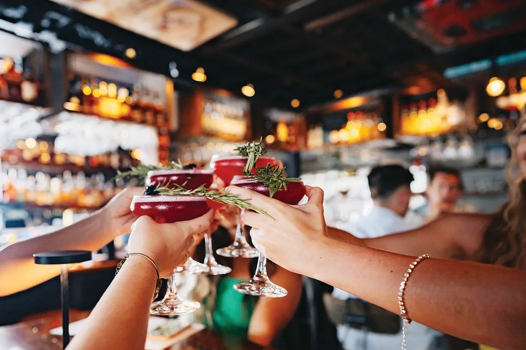 Picture of 4 hands holding mixed drinks and toasting each other in a circle at a bar