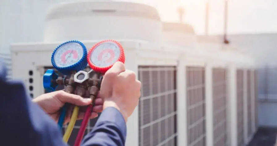Picture of two hands holding a HVAC gauge at an air conditioning unit