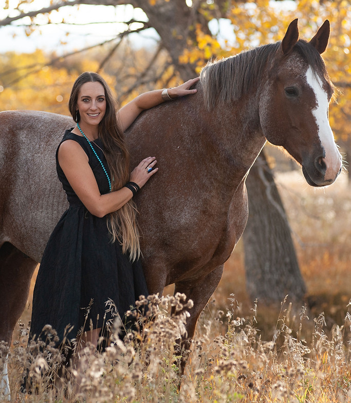 Women standing beside a horse in a field while she looks at the camera