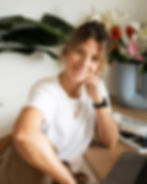 Ein Portrait von Franziska Heinl, sitzend an einem Tisch in einer lockeren Körperhaltung. Im Hintergrund sieht man Fachmagazine und Blumen.