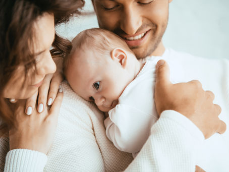 Baby in soft cotton clothing being hugged by caring parents