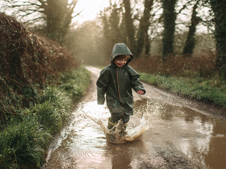 A child in a raincoat and wellies jumping in a puddle, representing PFAS-free water-repellent children’s outerwear.