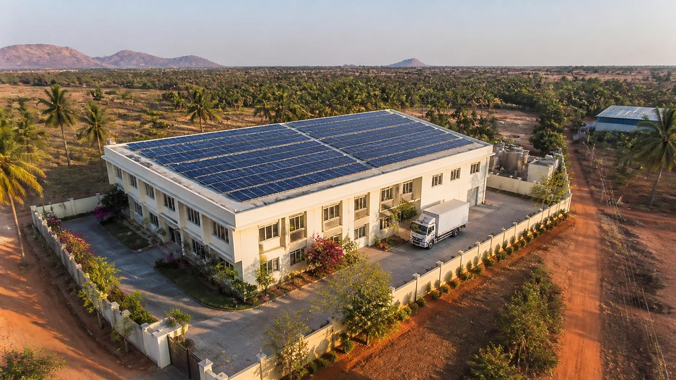 An aerial view of a two storey factory in southern India, its roof entirely covered with solar panels, water tanks to one side and a delivery truck in the forecourt, surrounded by red earth, palms and scrub. The kind of renewable electricity generation many suppliers installed years before their buyers asked. Illustrative image