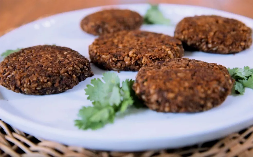 5 hamburgueres de feijão preto em cima de um prato branco com folhas de cebolinha enfeitando em seu entorno.