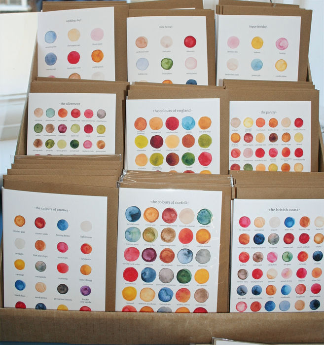 card stand with a selection of white greetings cards printed with different coloured paint samples representing different local areas around Norfolk and the UK and By Tilly branding