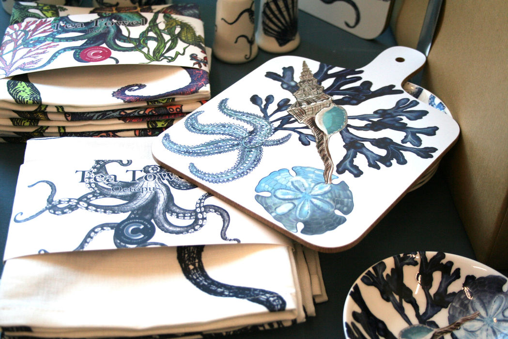 a selection of teatowels, cutting board, small dishes and coasters all white and printed with navy, purple and green realistic images of octopus, shells, coral and starfish