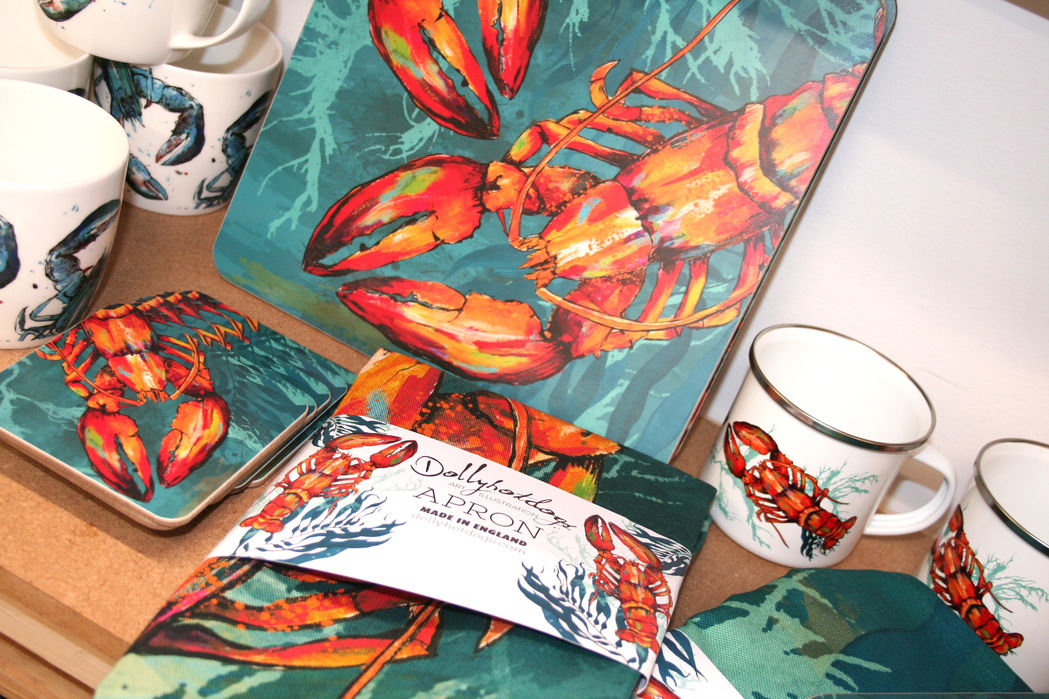coasters and apron with teal green background and bright orange and red printed realistic lobster design alongside a white enamel mug with the same lobster motif with Dollyhotdogs branding