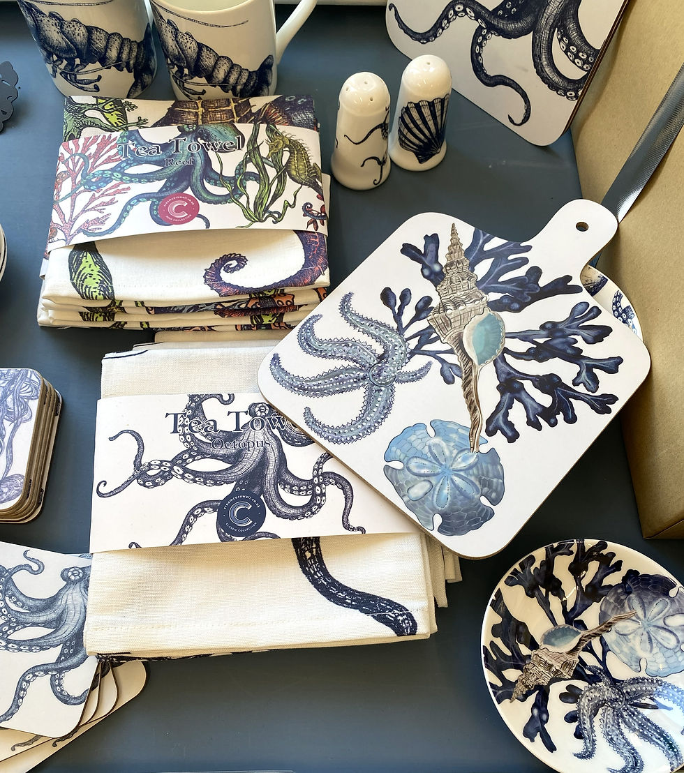 Selection of white teatowels with navy blue, royal purple and Dark green realistic octopus printed, with a white decorative cutting board printed with navy blue realistic coral, sand dollar and starfish.