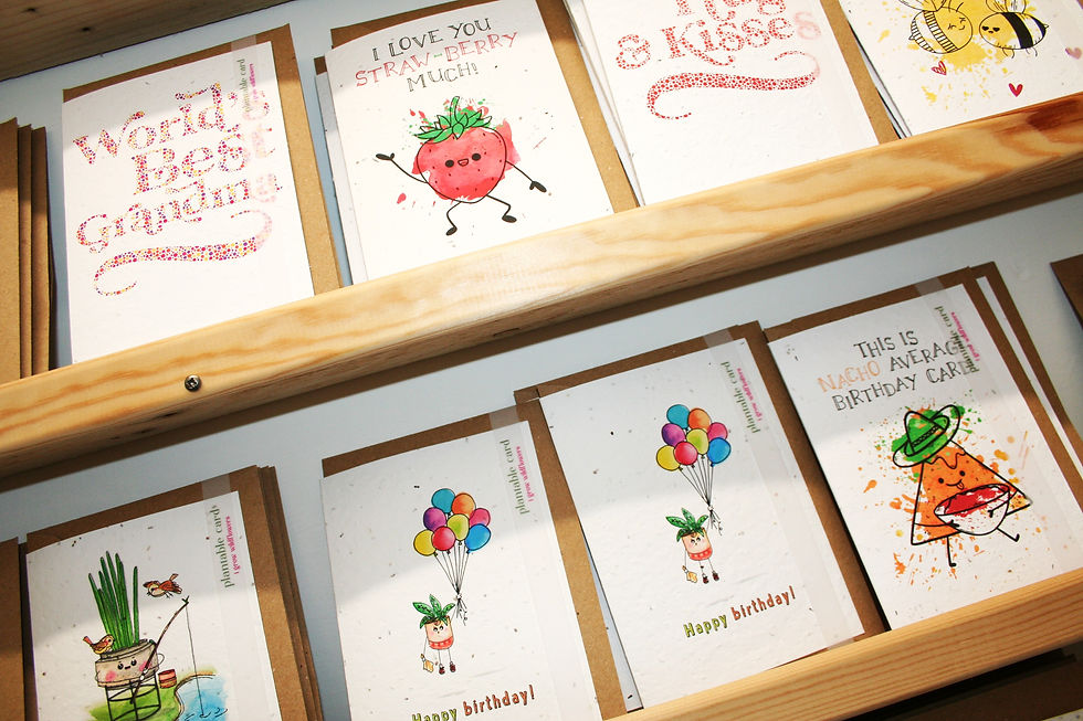 wooden shelf with off white greetings cards with colourful hand decorated designs featring strawberries and messages such as 'Hugs and Kisses' and The Seed Card Company branding