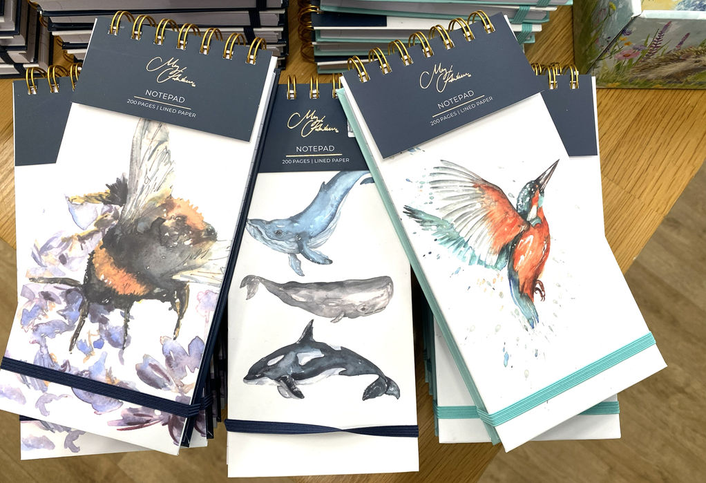 three narrow top ring bound notebooks, one with watercolour bumblebee, one with three watercolour whales and one with watercolour kingfisher all with Meg Hawkins Art branding