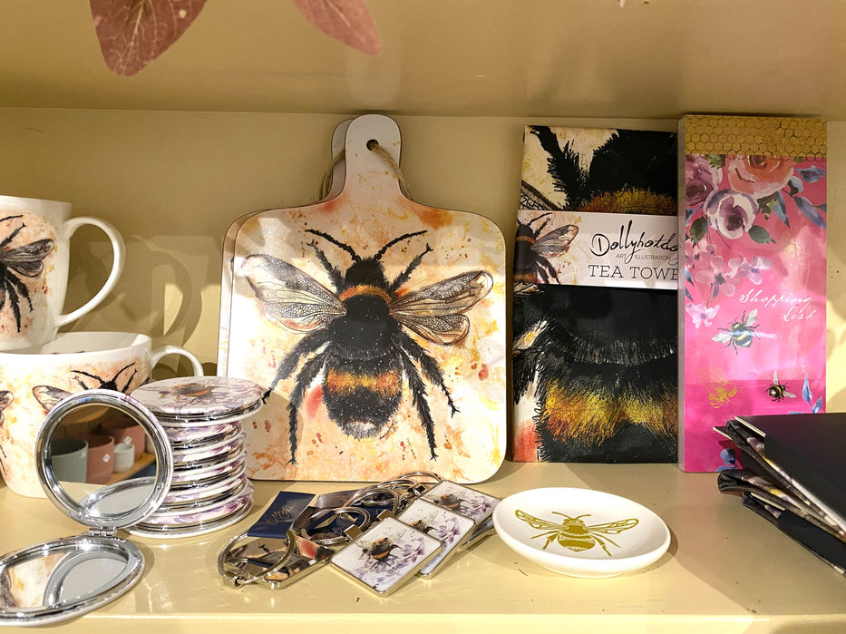 cream cutting board with large realistic bumblebee design, alongside keyrings and small  round folding mirrors printed with the same design with Dollyhotdogs branding