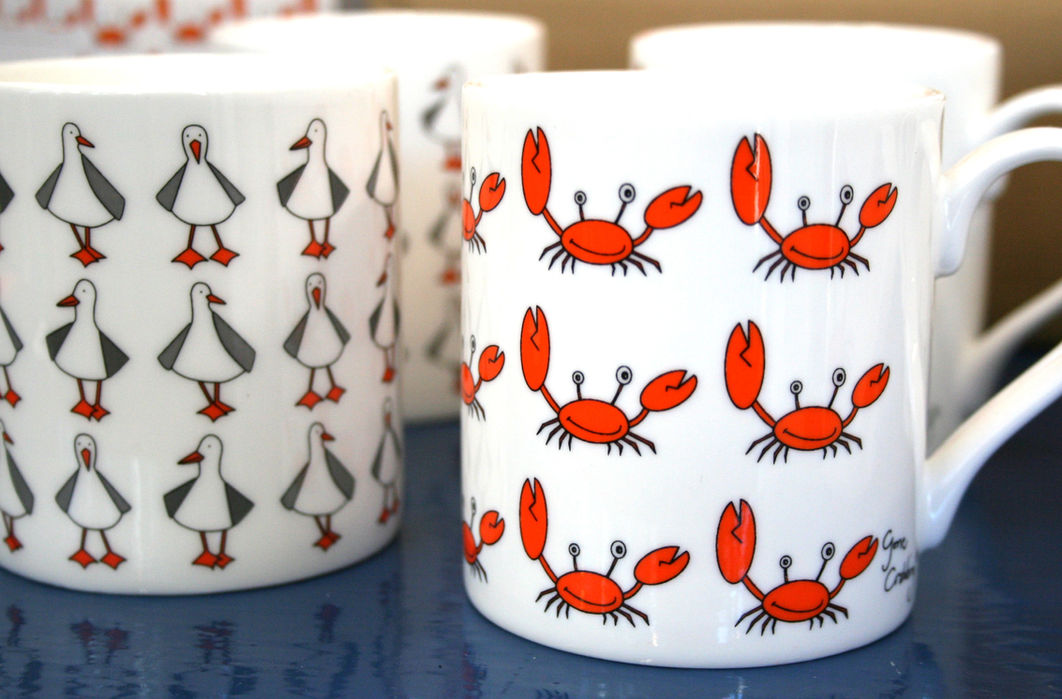 two while china mugs, one with seagulls printed on and the other with cheerful orange crabs and Gone Crabbing branding