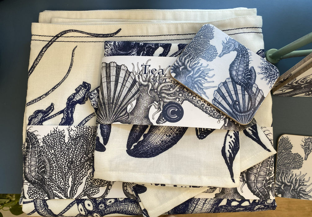 selection of tablecloth, teatowel, and coasters with navy blue realistic images of seahorse, coral, lobster and sea anemones