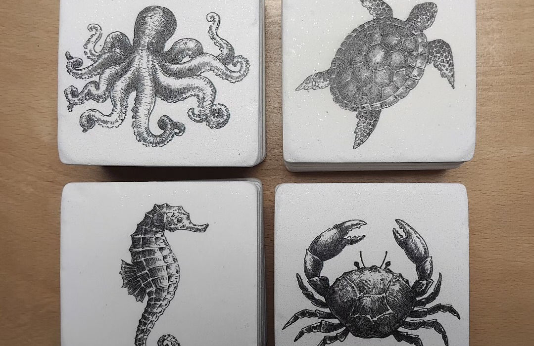 four white ceramic coasters with navy blue realistic line drawings of sea creatures