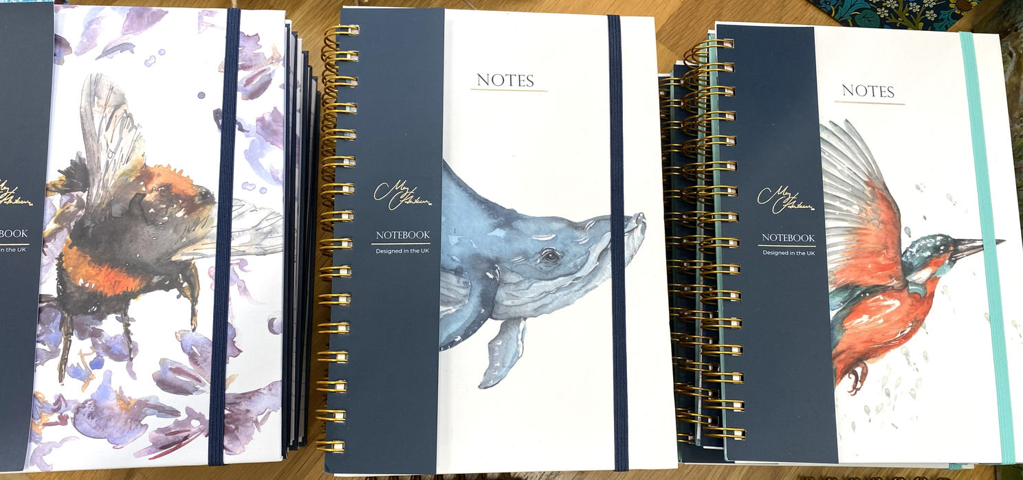 three A5 side ring bound notebooks, one with watercolour bumblebee, one with watercolour whale and one with watercolour kingfisher all with Meg Hawkins Art branding