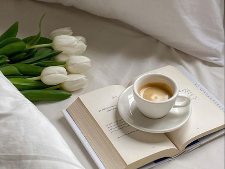 Cama com objetos sobre ela, um livro, uma xícara de café e um buque de tulipas
