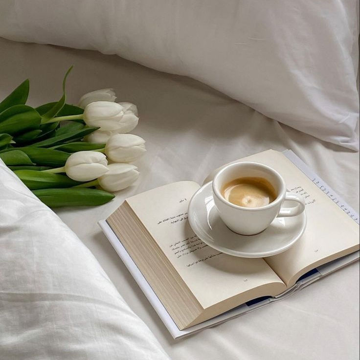 Cama com objetos sobre ela, um livro, uma xícara de café e um buque de tulipas
