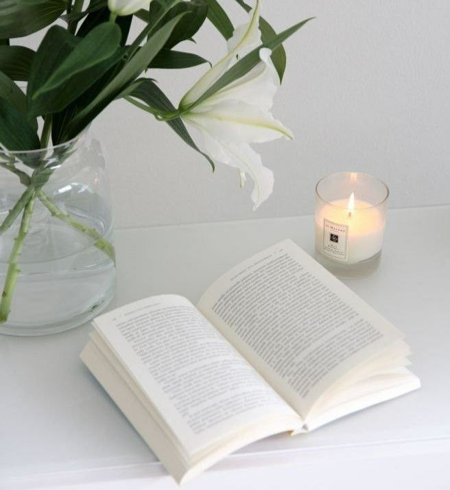 livro, jarro de flores e uma vela